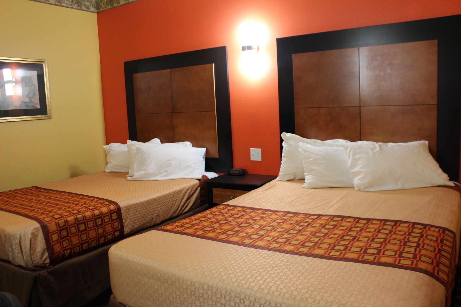 Two single beds with headboards, a nightstand, and a wall-mounted light fixture in a hotel room.