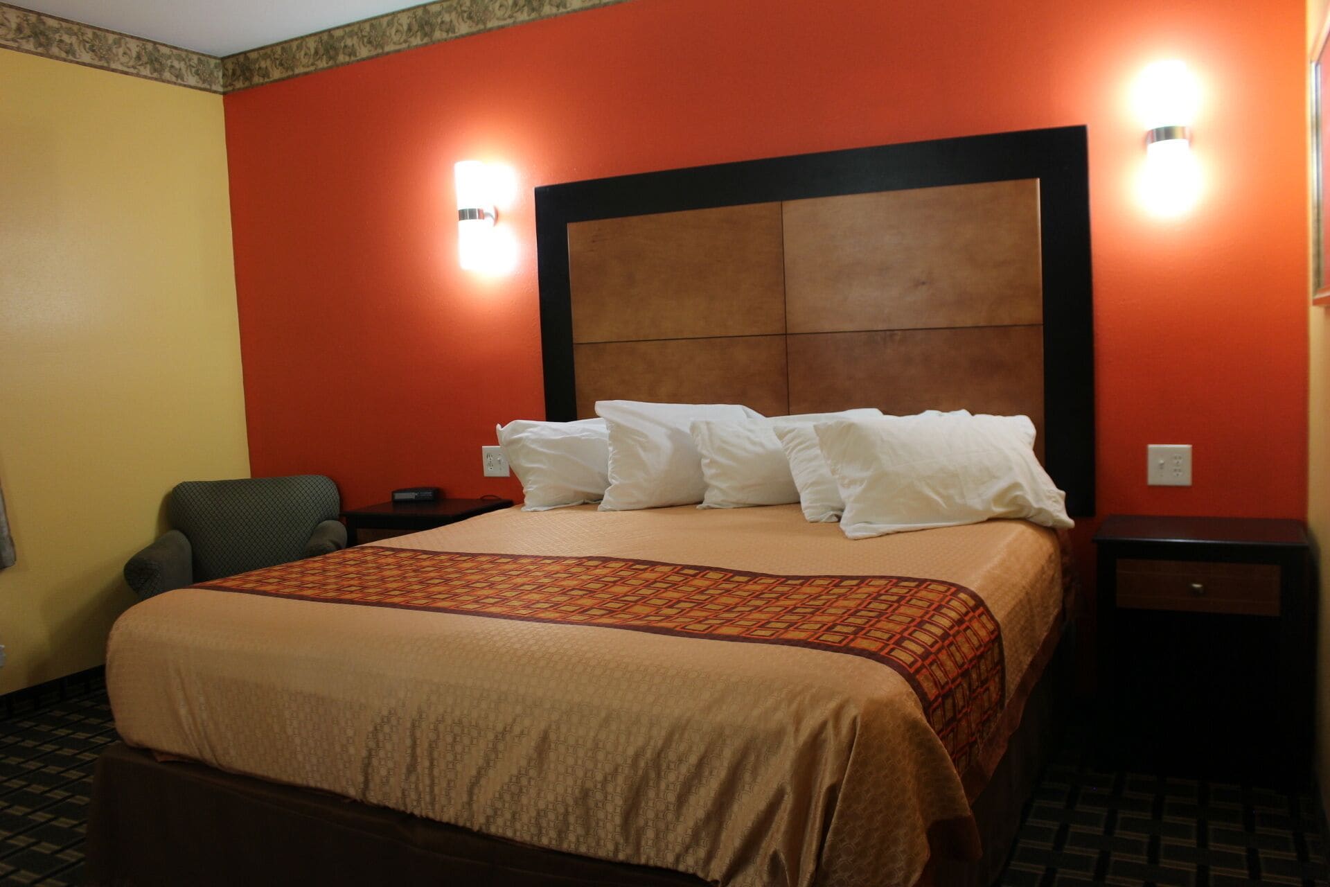 A hotel room with a large bed, two bedside tables, a chair, and a wall-mounted light fixture.