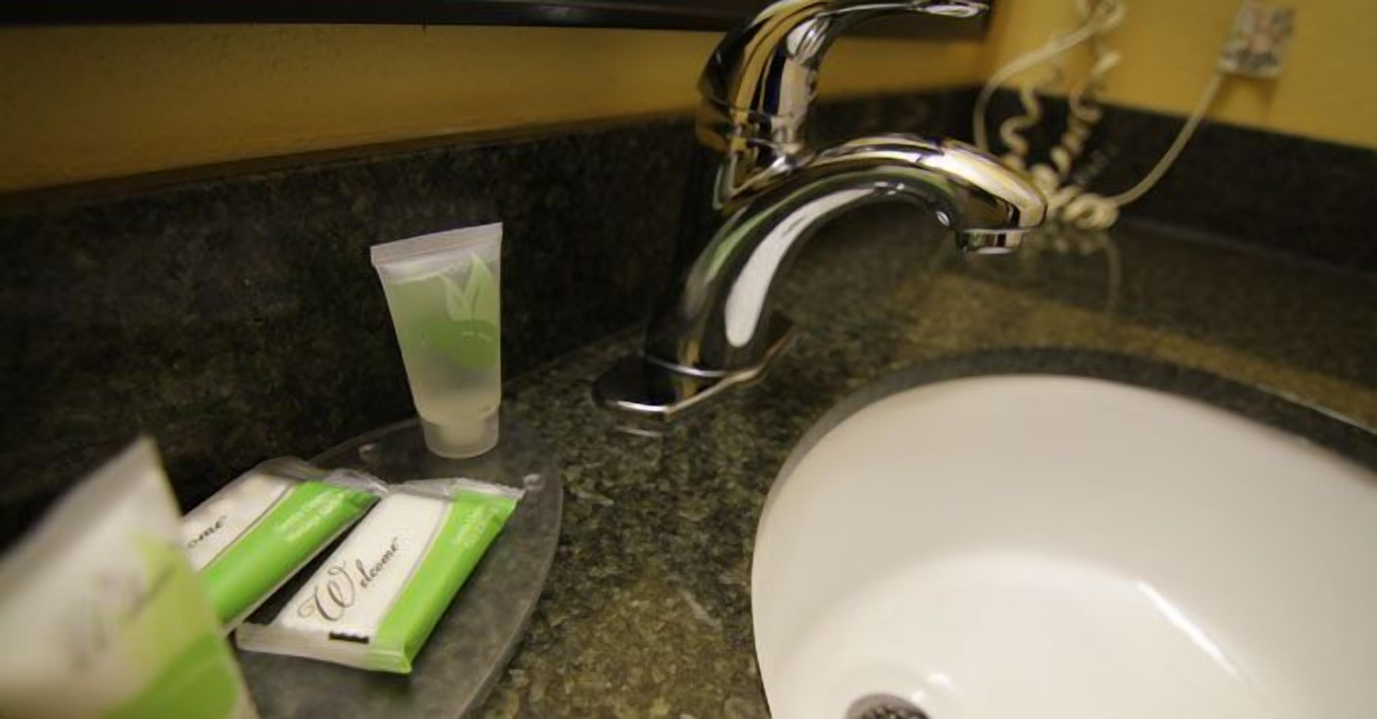 Un lavamanos con grifo cromado, un lavabo blanco y un paquete de artículos de tocador verde y blanco sobre la encimera.