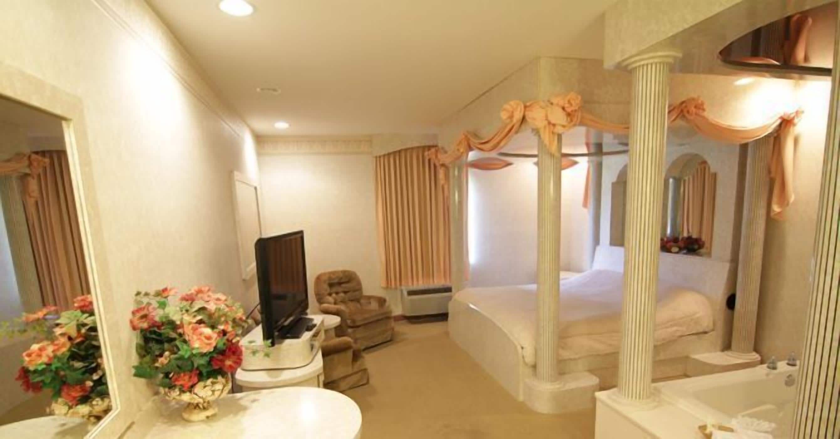 A hotel room with a large bed, a sitting area with a TV, and a bathroom with a bathtub.