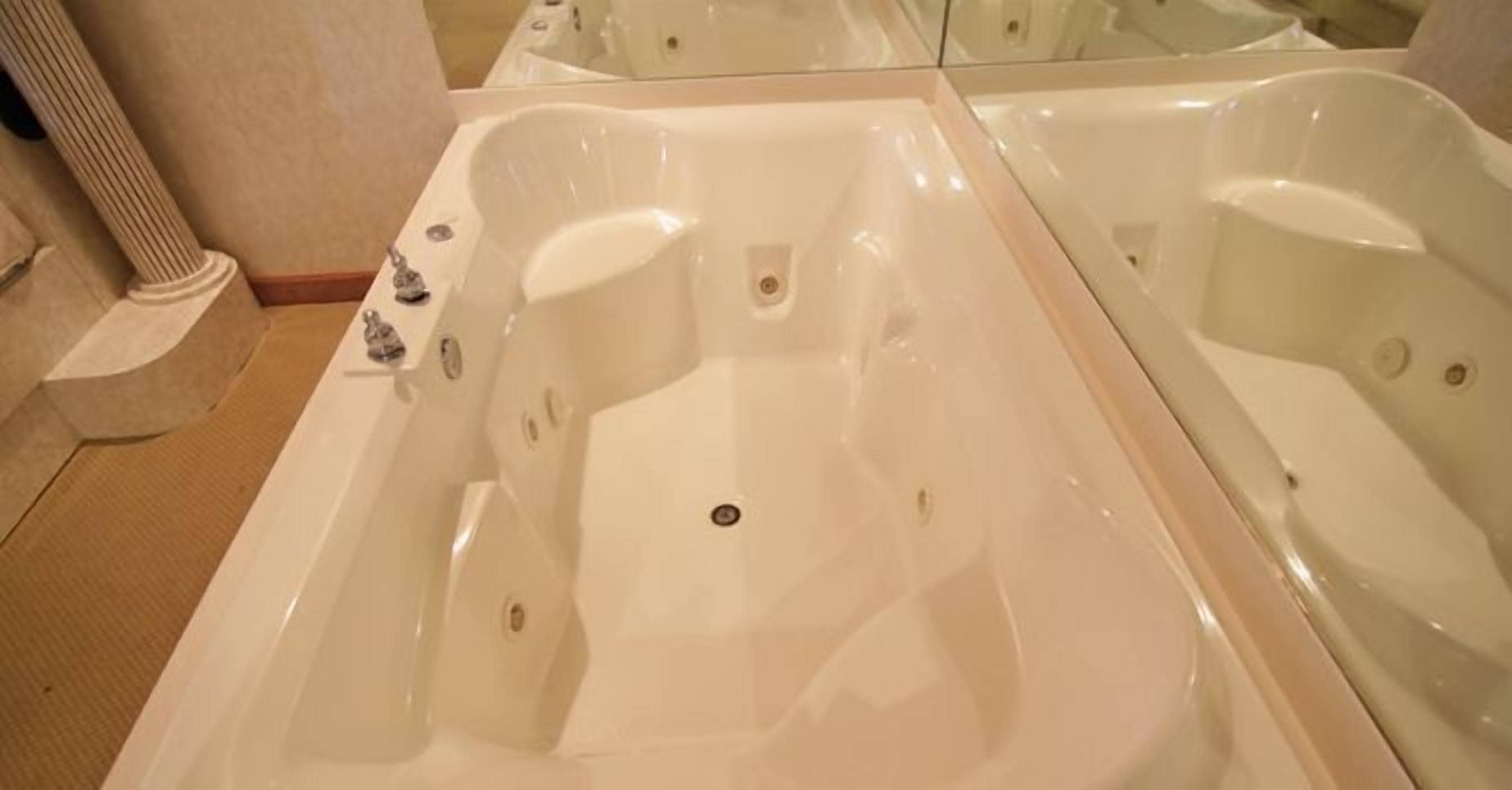 A large, empty bathtub with a drain in the center, surrounded by a beige floor and a column.