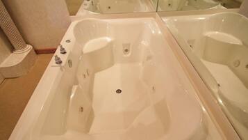 A large, empty bathtub with a drain in the center, surrounded by a beige floor and a column.