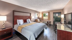 A hotel room with a large bed, bedside tables, a desk, a chair, a TV, and a door. - Colonial Inn (Camden)