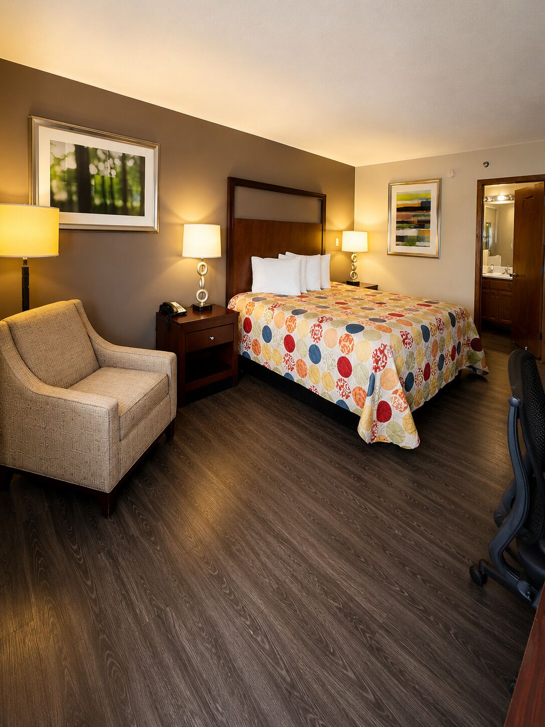 A hotel room with a bed, two bedside tables, a chair, a desk, and a desk lamp.