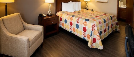 A hotel room with a bed, two bedside tables, a chair, a desk, and a desk lamp.