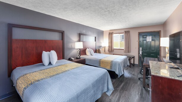 A hotel room with two beds, a desk, a chair, a TV, and a door. - Colonial Inn (Camden)