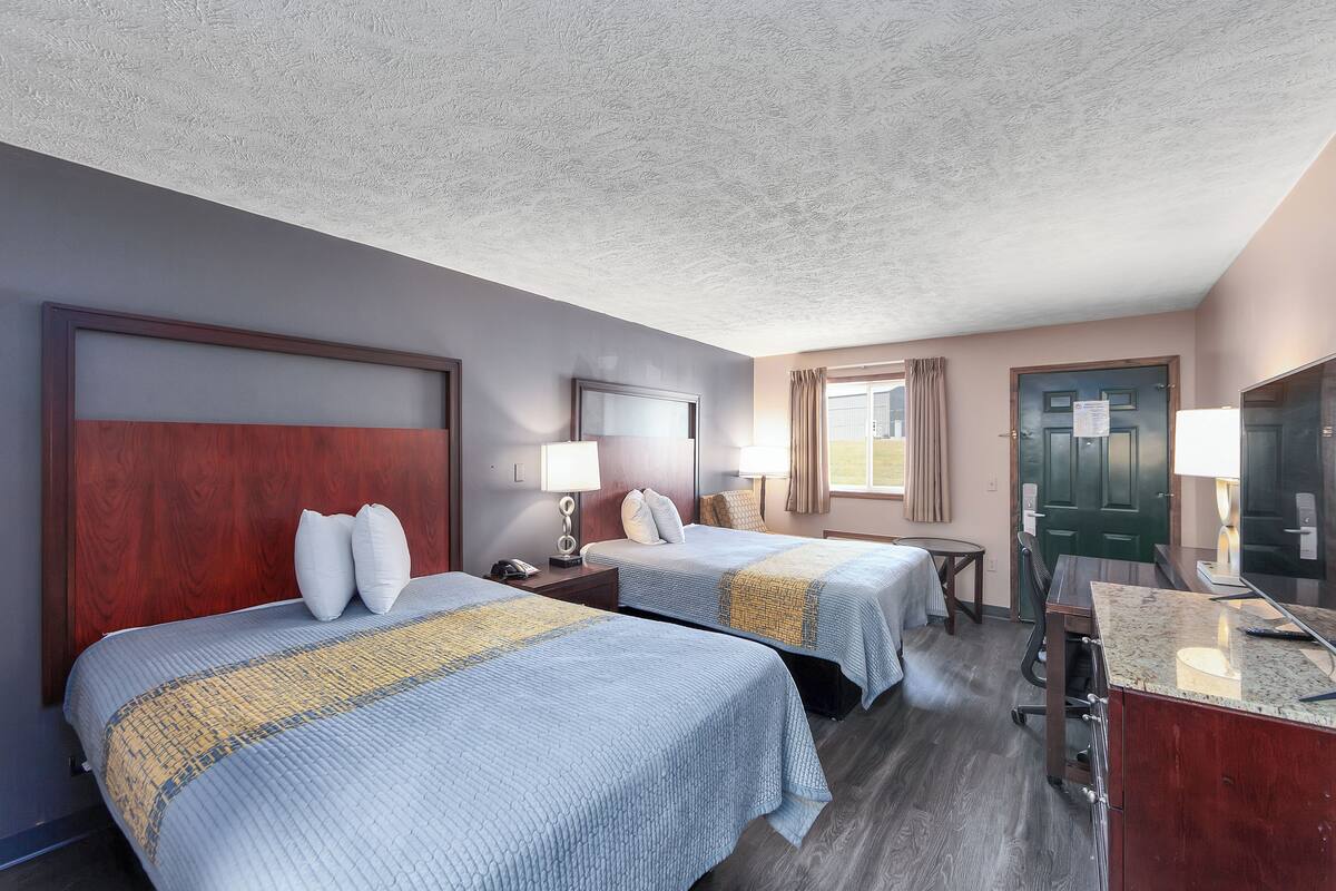 A hotel room with two beds, a desk, a chair, a TV, and a door.