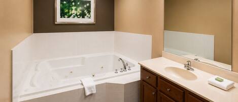 A bathroom with a bathtub, vanity, mirror, and recessed lighting.