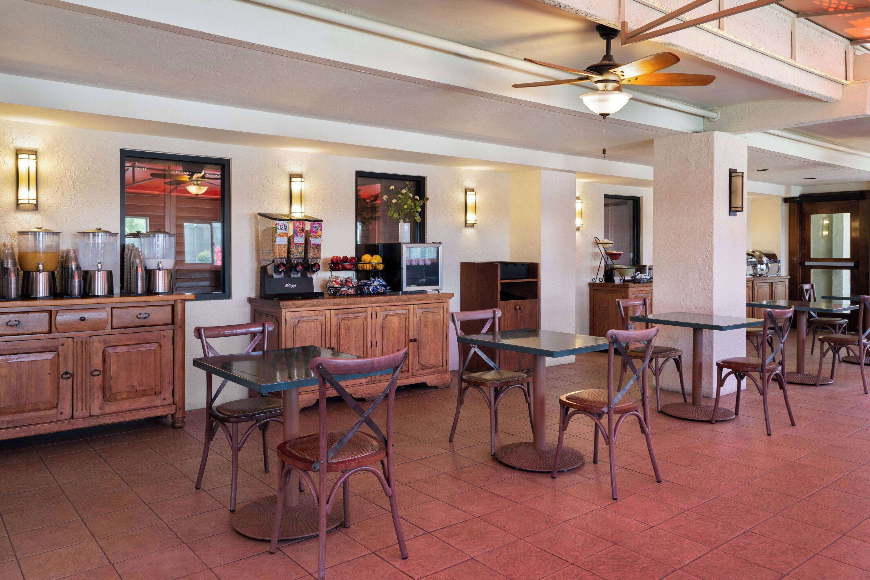 A spacious indoor area with wooden cabinets, a coffee station, and several tables and chairs.