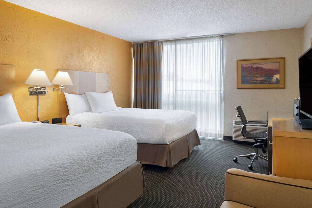 A hotel room with two beds, a desk, a chair, a television, and a painting on the wall.