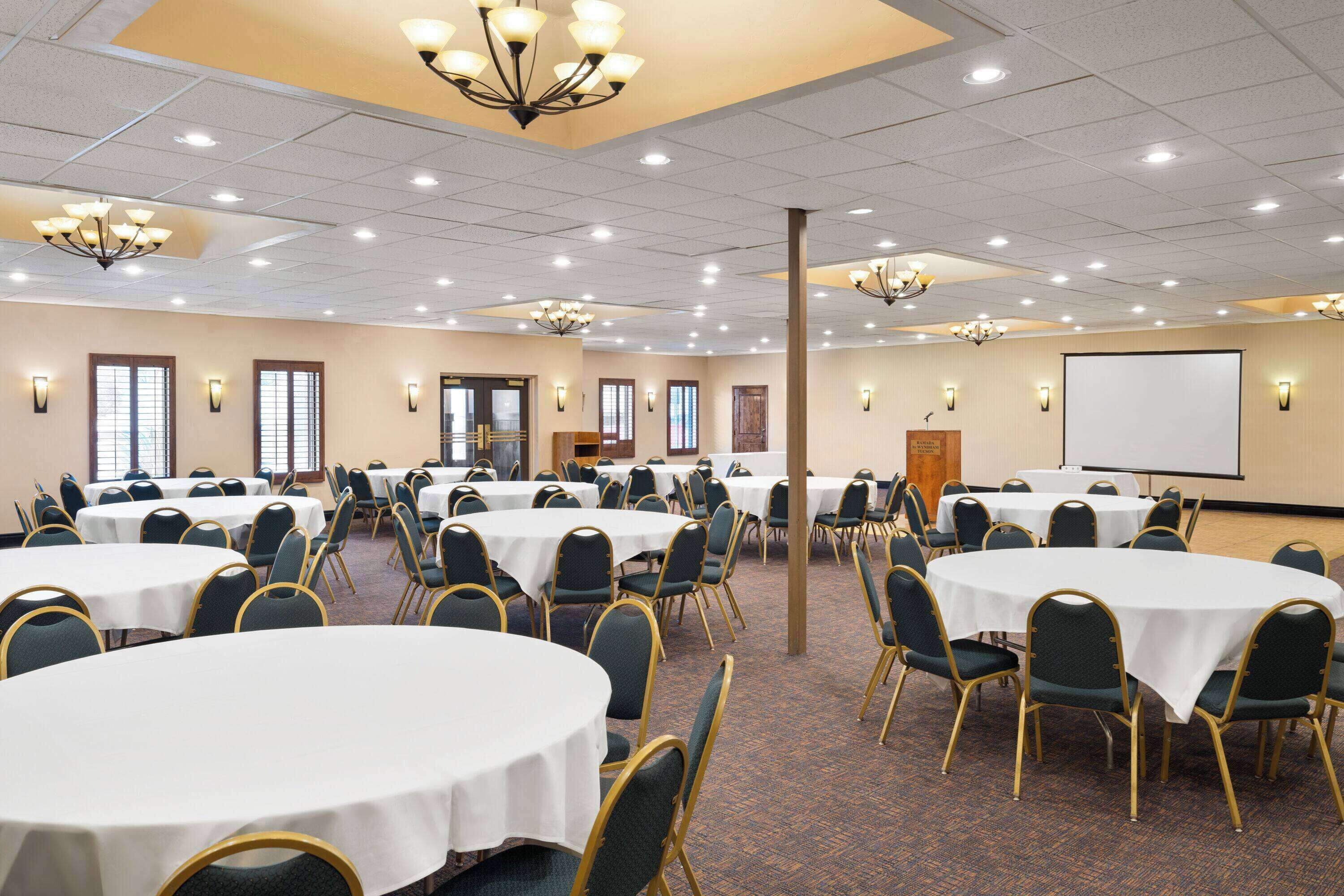A conference room with multiple round tables, chairs, and a projector screen.