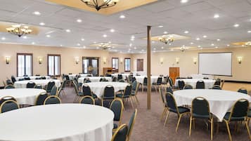 A conference room with multiple round tables, chairs, and a projector screen.