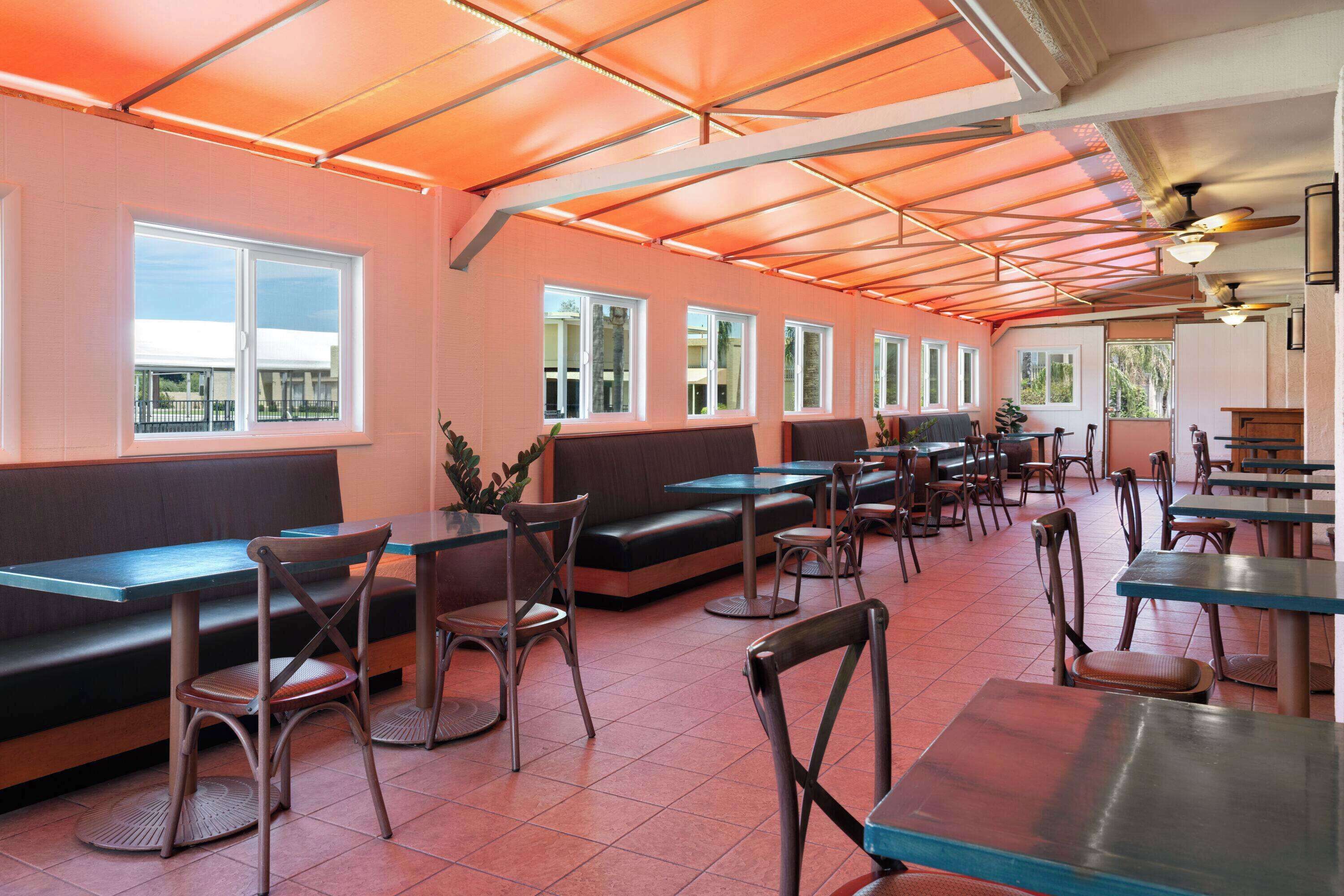 Un restaurant avec des banquettes et des tables, de grandes fenêtres et un plafond orné de panneaux orange.