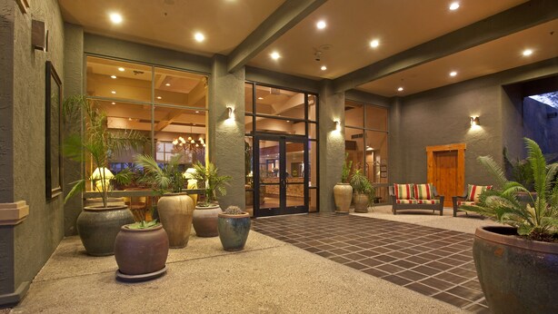 A hotel lobby with large potted plants, a seating area with striped cushions, and a tiled floor. - Ramada by Wyndham Tucson (Tucson)