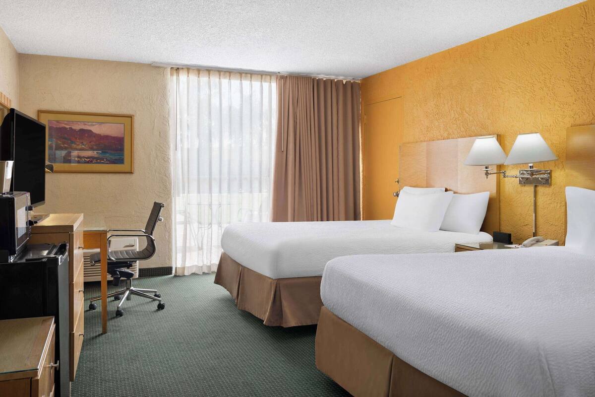 A hotel room with two beds, a desk with a chair, a television, and a painting on the wall.