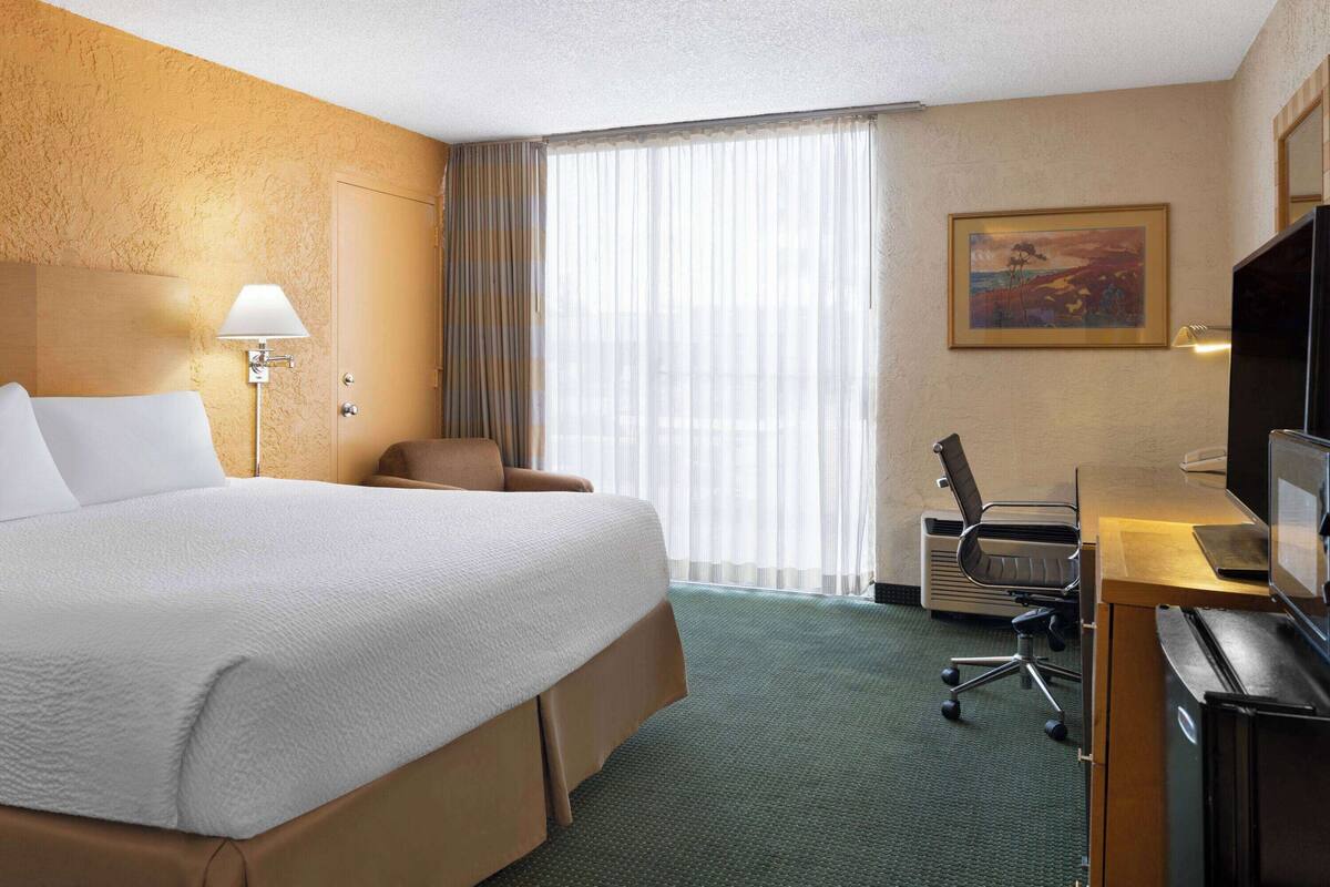 A hotel room with a large bed, a desk with a computer, a chair, and a television.