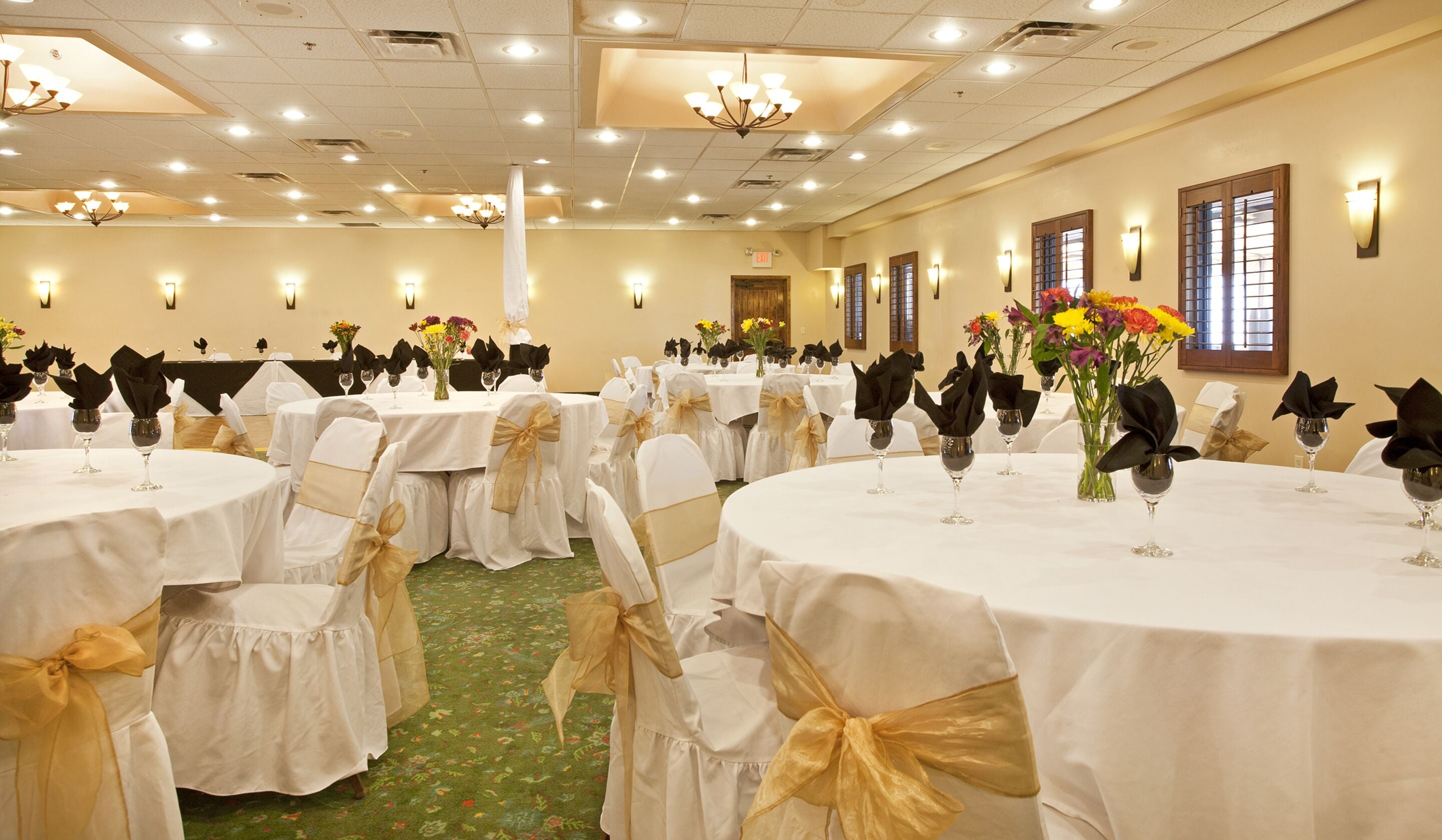 A banquet hall with round tables, chairs with gold sashes, and floral centerpieces.