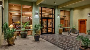 A hotel lobby with a tiled floor, potted plants, a bench, and a reception area with a glass door. - Ramada by Wyndham Tucson (Tucson)