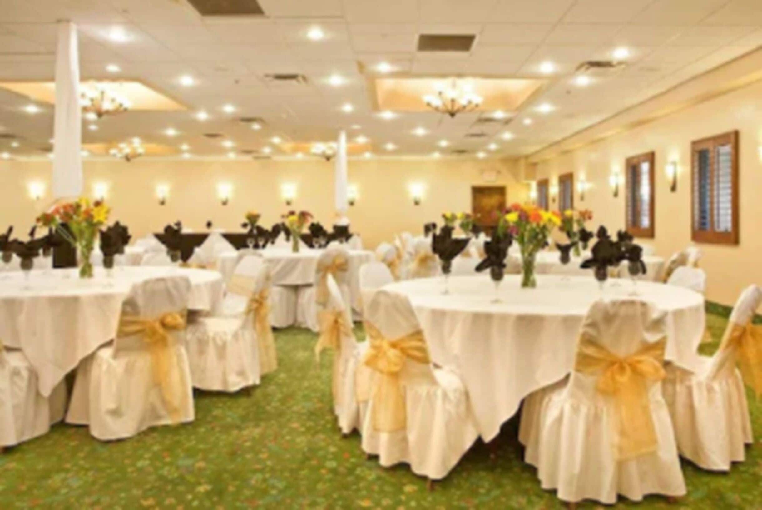 A banquet hall with round tables, each with a white tablecloth and gold sashes, and chairs with matching sashes.