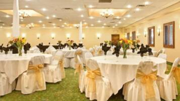 A banquet hall with round tables, each with a white tablecloth and gold sashes, and chairs with matching sashes.