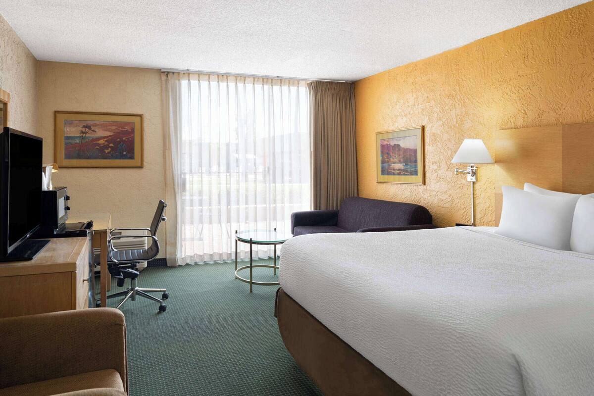 A hotel room with a large bed, a desk with a computer, a chair, a small table, and two paintings on the walls.