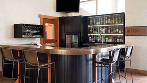 A bar area with a counter, bar stools, a television, and a liquor display. - Ramada by Wyndham Tucson (Tucson)