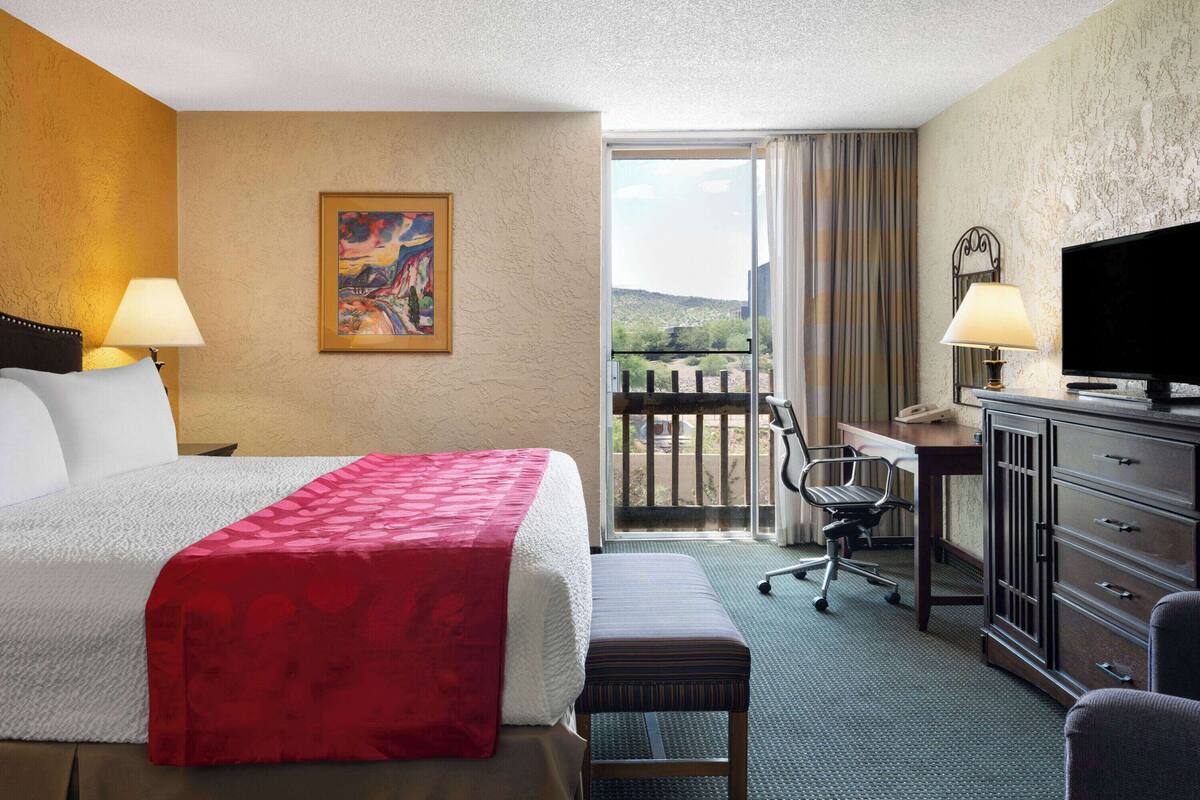 A hotel room with a bed, a desk, a television, and a balcony with a view.