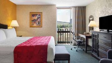Une chambre d’hôtel avec un lit, un bureau, une télévision et un balcon offrant une vue.