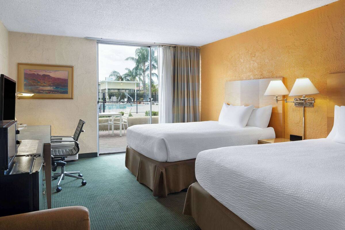 A hotel room with two beds, a desk, a chair, and a television.