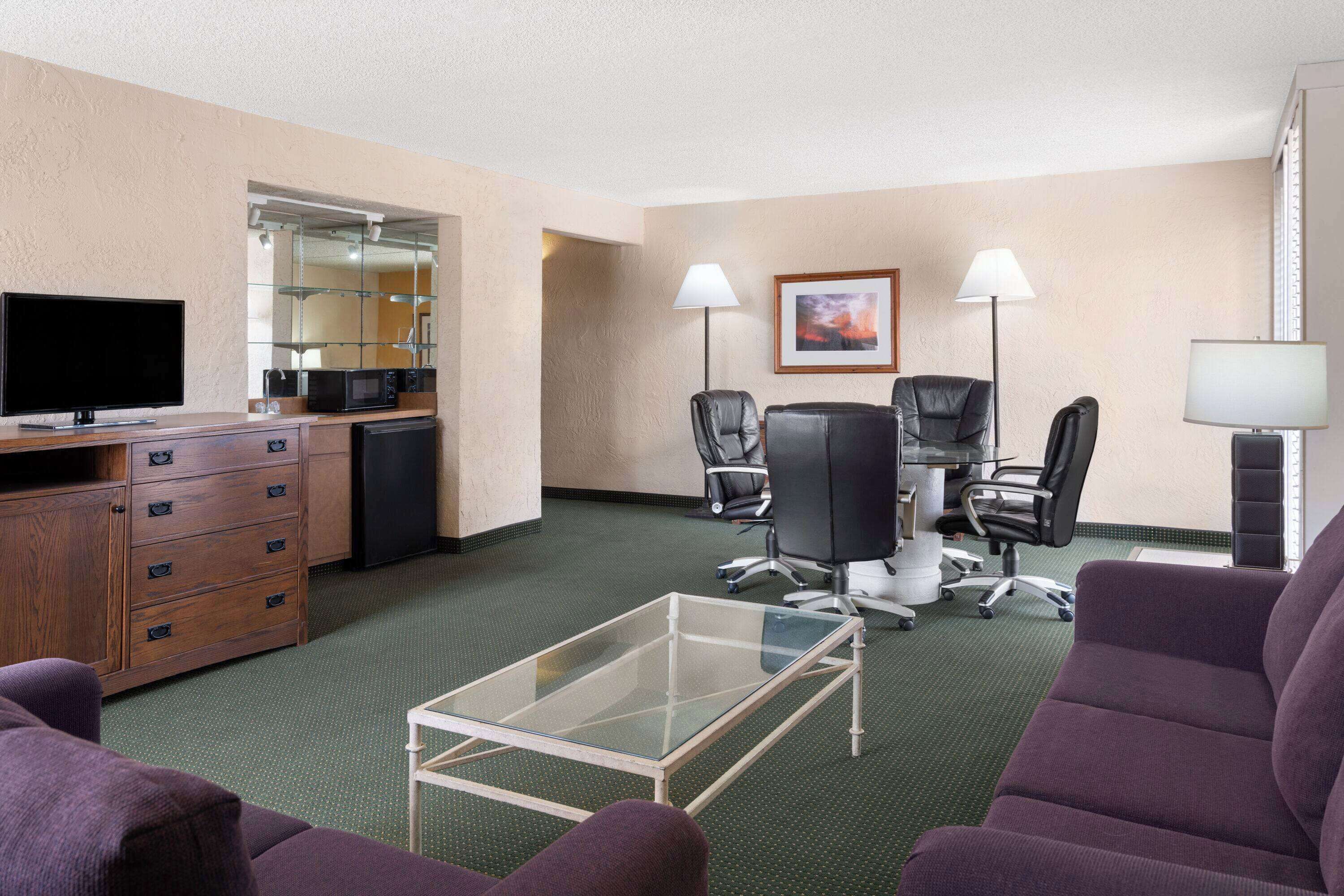 Ein Hotelzimmer mit Fernseher, Mikrowelle und einer kleinen Küchenzeile. In der Mitte befinden sich zwei Stühle und ein Tisch, und im Vordergrund ein Sofa.