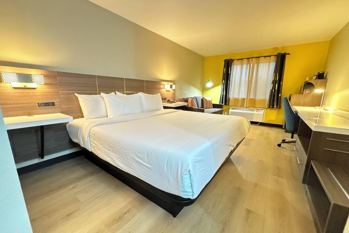A modern hotel room with a large bed, a desk, and a chair.