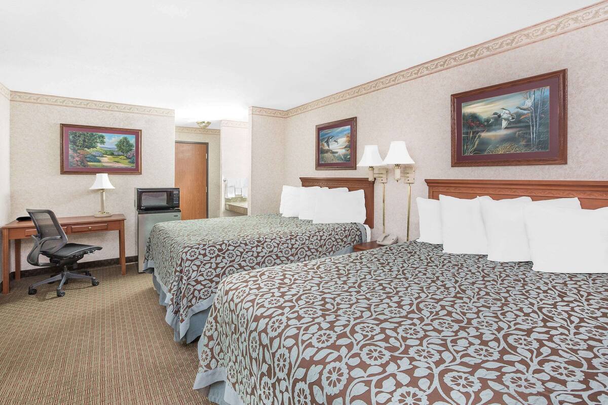 A hotel room with two beds, a desk with a computer, a chair, and a TV.