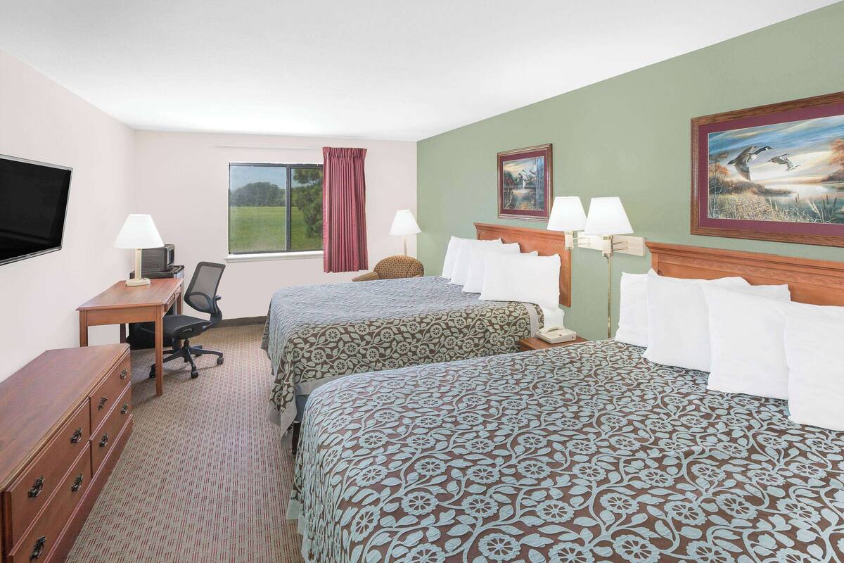 A hotel room with two beds, a desk, a chair, a TV, and a window with a view of the outdoors.