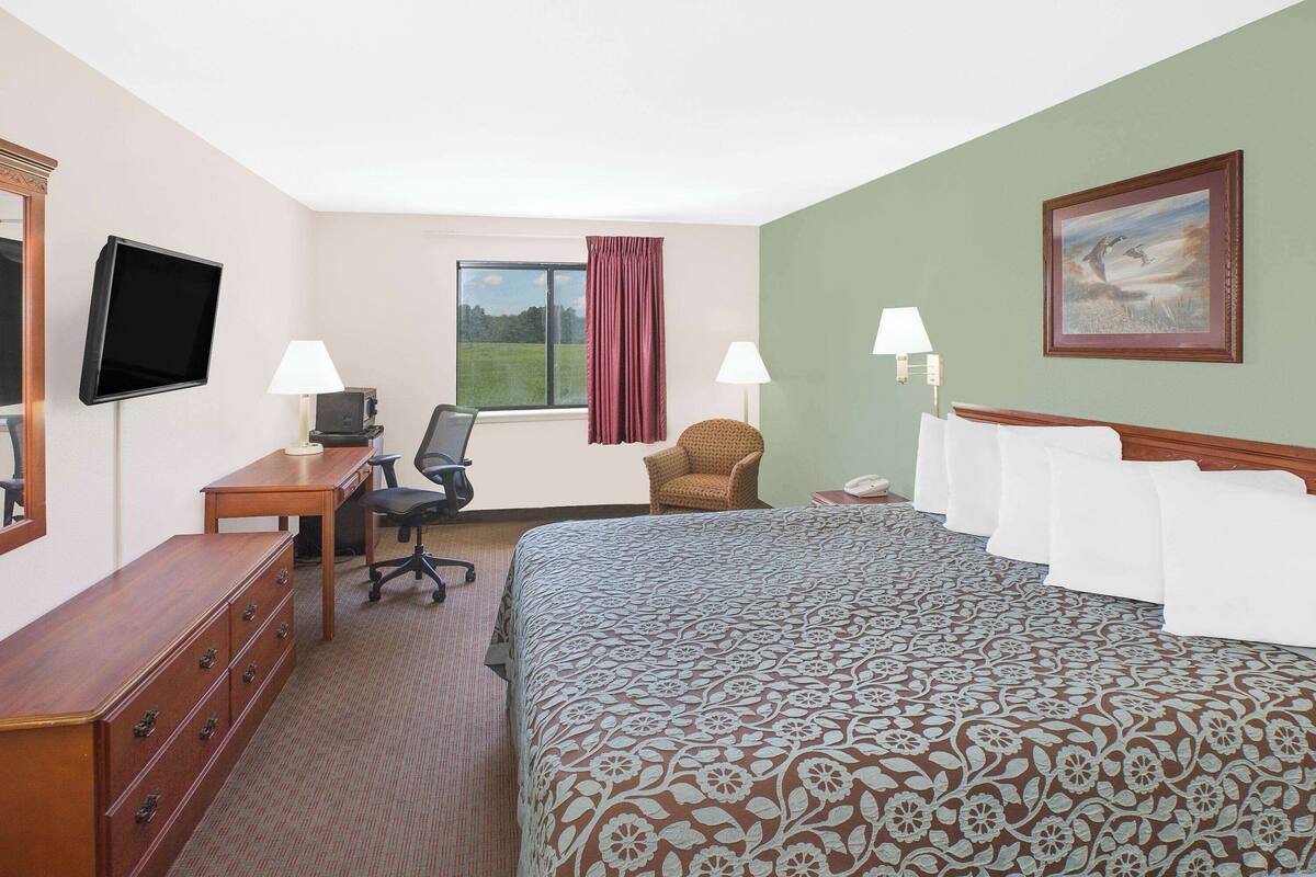 A hotel room with a bed, a desk, a chair, a TV, and a window with curtains.