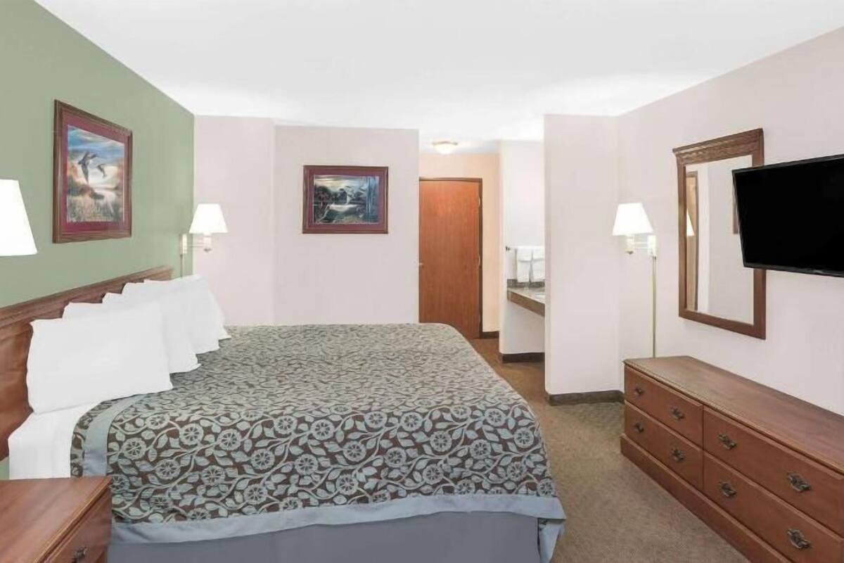 A hotel room with a bed, a dresser, a television, and two paintings on the walls.