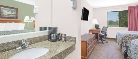 A hotel room with a granite countertop sink, a bed with a patterned bedspread, a desk with a chair, a television, and a window with curtains.