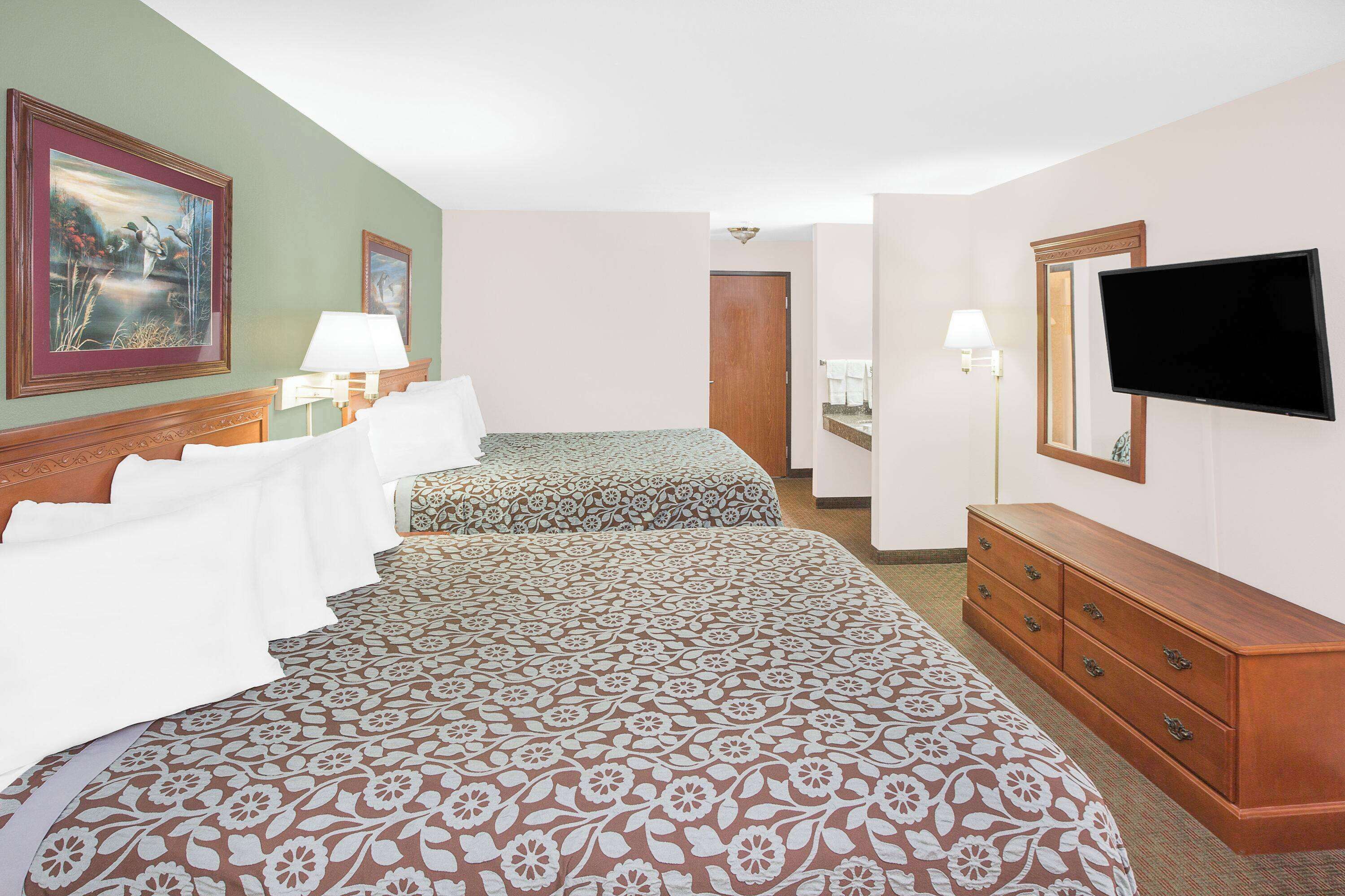 A hotel room with two beds, a dresser, a TV, and artwork on the walls.