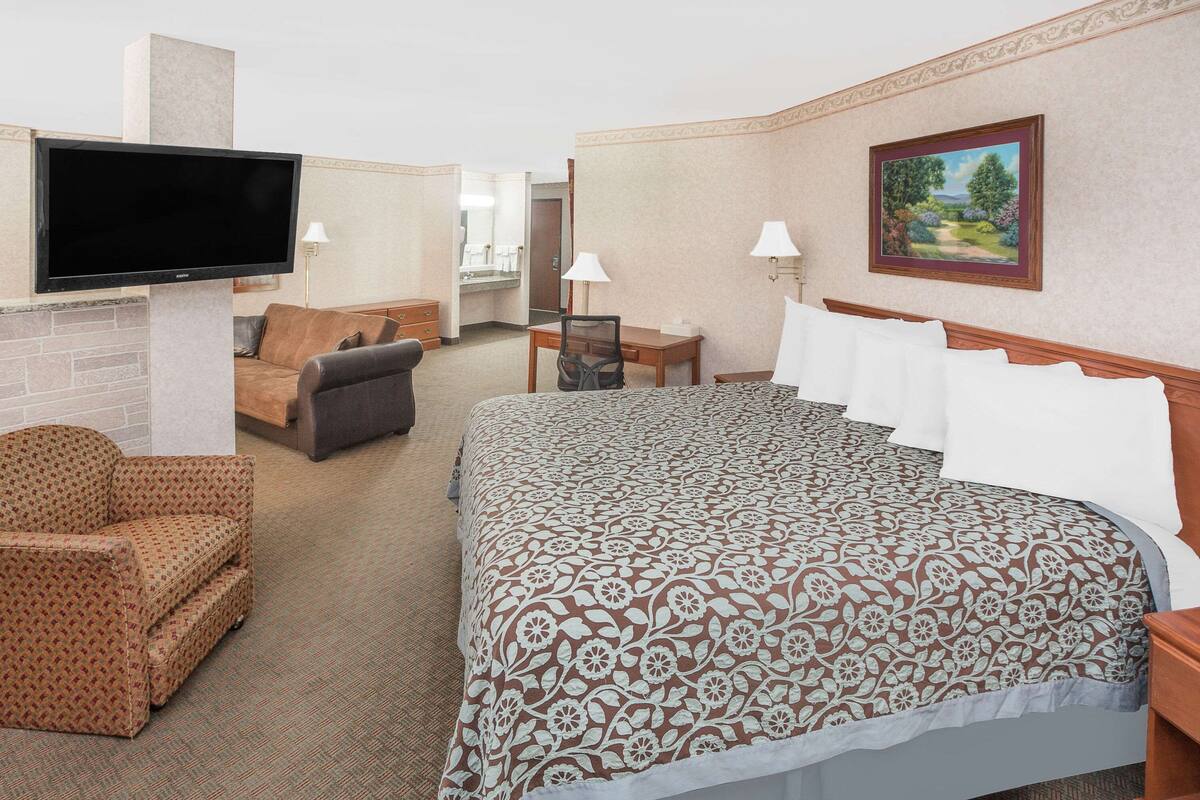 A hotel room with a large bed, a TV, a sofa, a desk, and a painting on the wall.