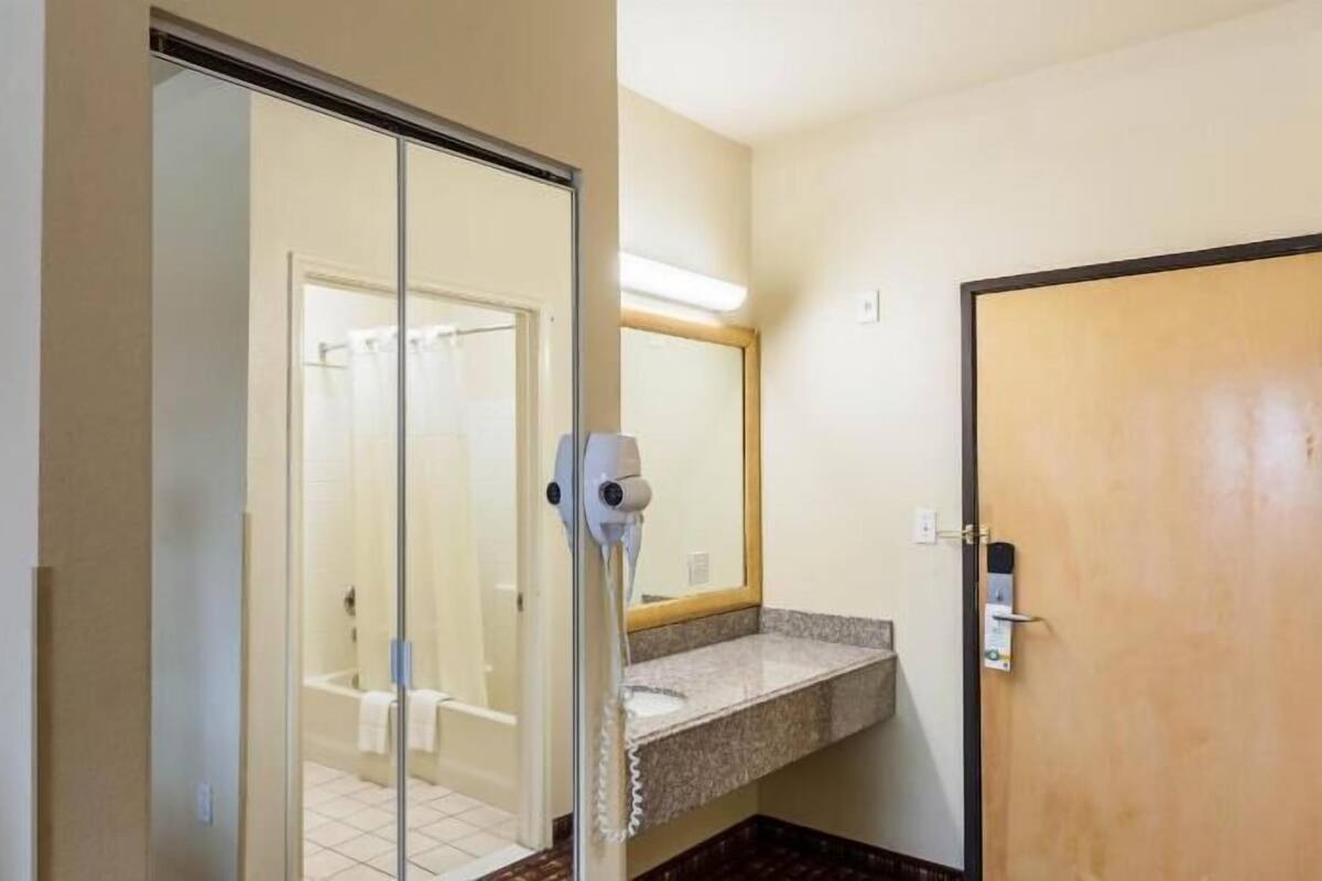 A hotel bathroom with a glass door leading to a shower, a sink with a towel, and a mirror.