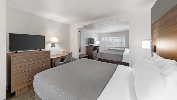 A hotel room with a bed, a desk with a computer, a television, and a window with blinds. - Quality Inn near SeaWorld - Lackland (San Antonio)