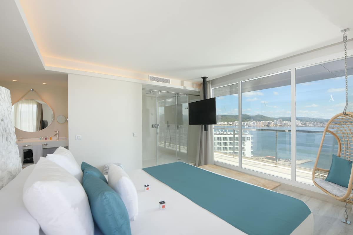 Quarto de hotel moderno com uma cama grande, televisão e varanda vista para o mar.