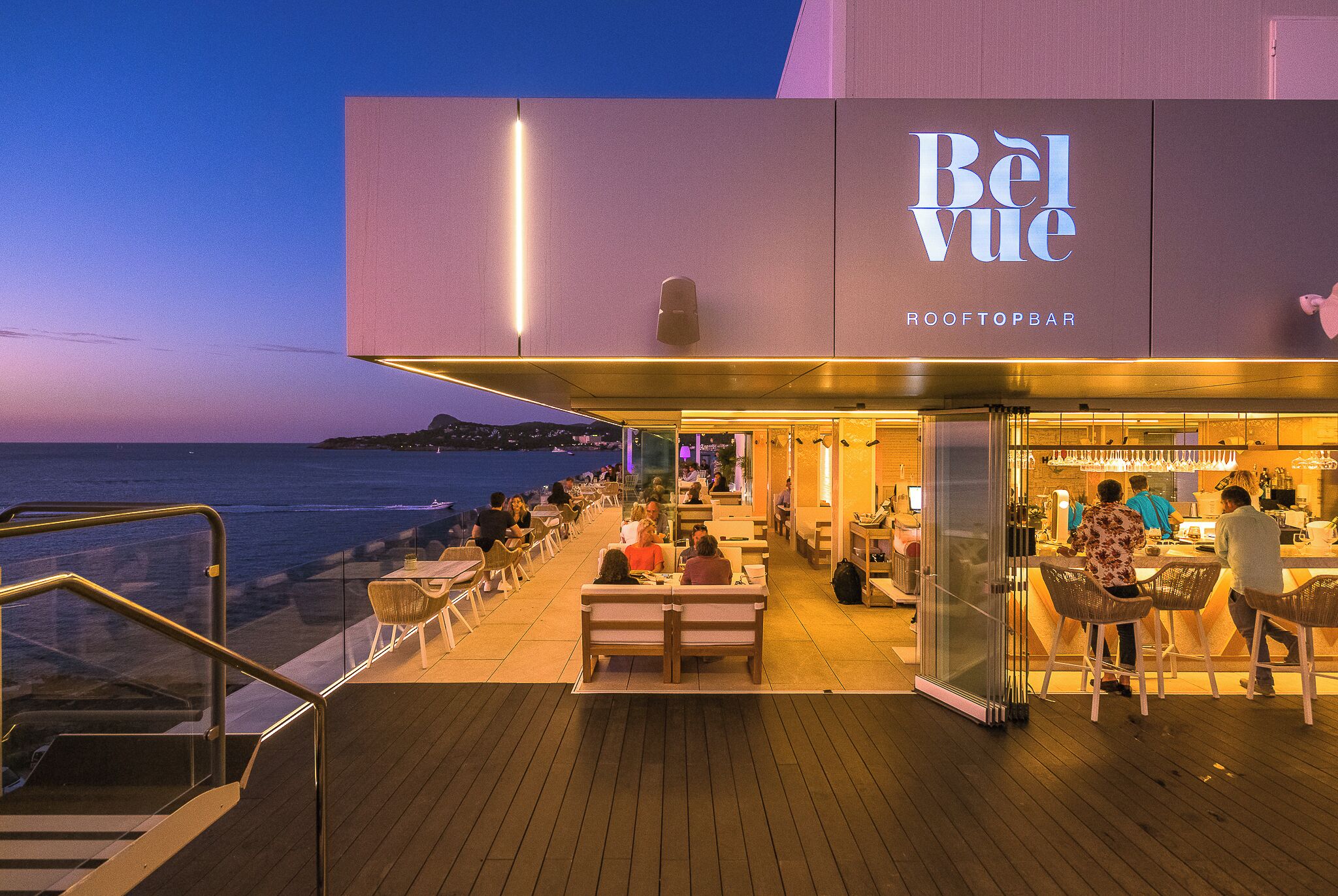 A rooftop bar named 'Bel Vue' with outdoor seating and a view of the sea.