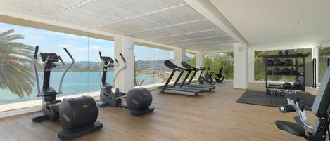 Un gimnasio espacioso con máquinas de cardio, equipo de levantamiento de pesas y vistas al mar.