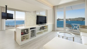 Ein modernes Wohnzimmer mit großem Fernseher, einer Couch und einem Balkon mit Meerblick.