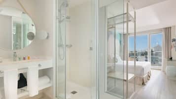 A modern bathroom with a glass-enclosed shower, a large mirror, and a vanity with toiletries.