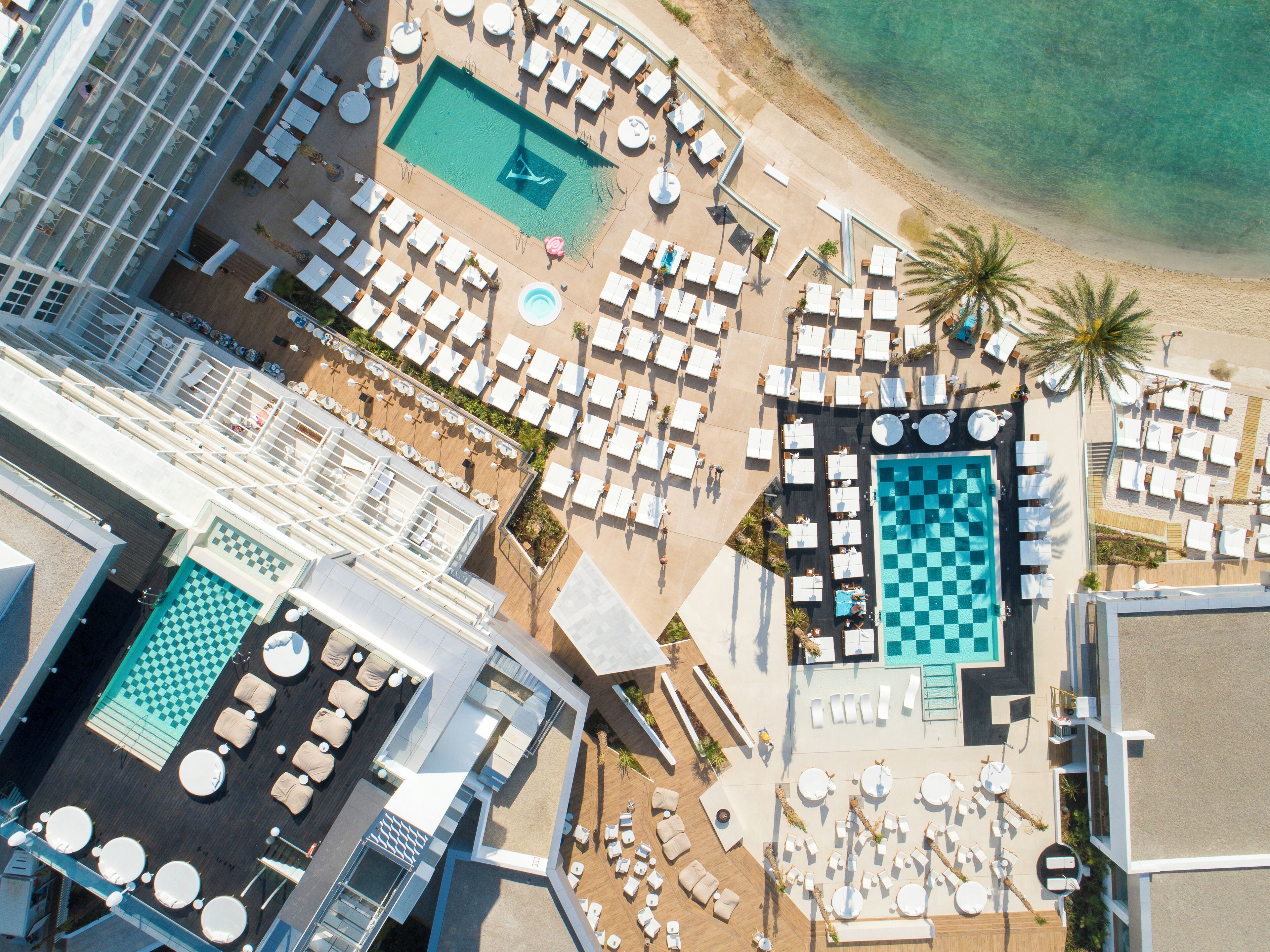 Vista aérea de un complejo turístico con varias piscinas, tumbonas y una zona de playa.