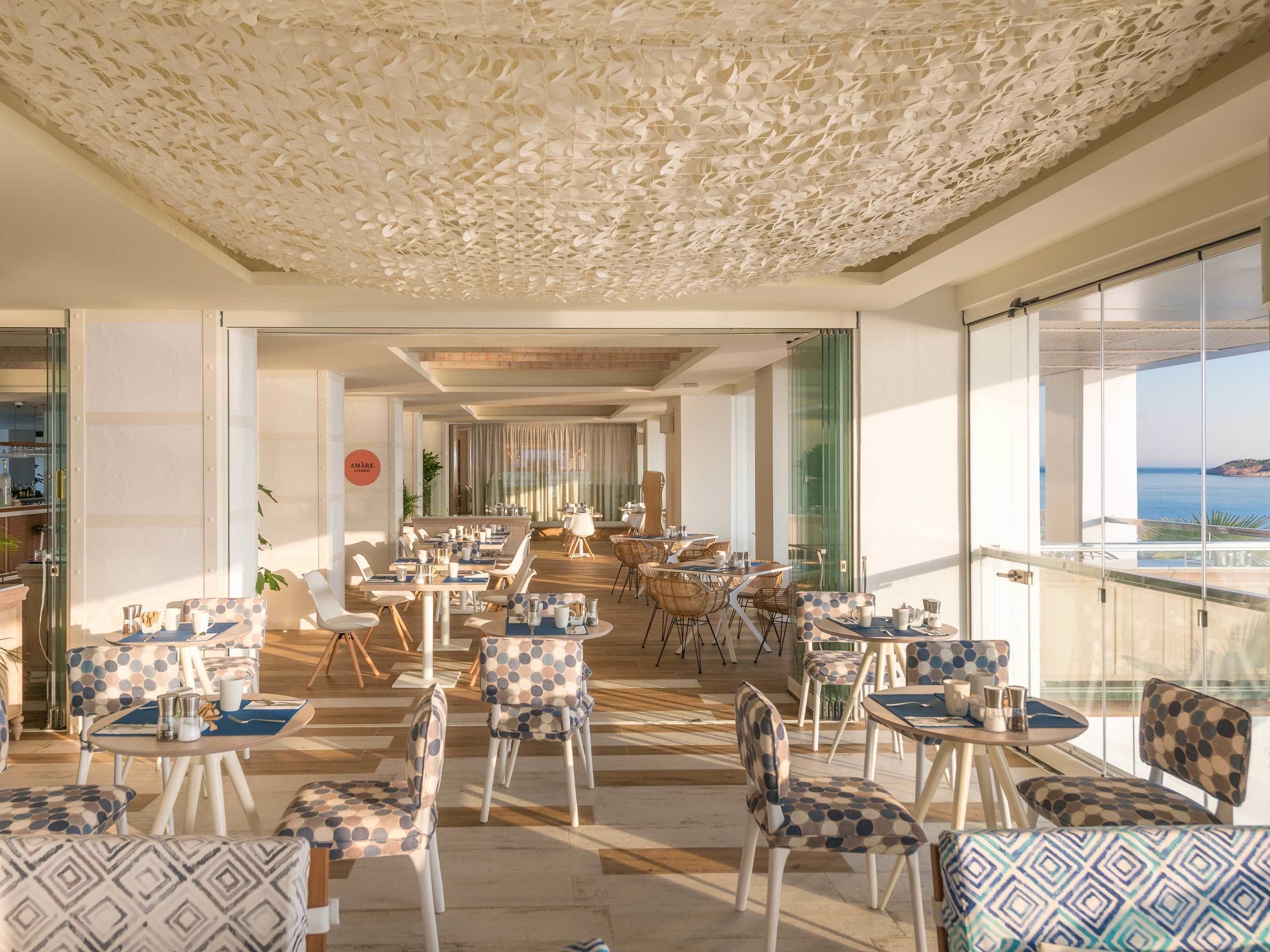Un amplio espacio comedor al aire libre con sillas y mesas estampadas, techo decorativo y vista al mar.
