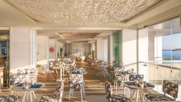 Un amplio espacio comedor al aire libre con sillas y mesas estampadas, techo decorativo y vista al mar.