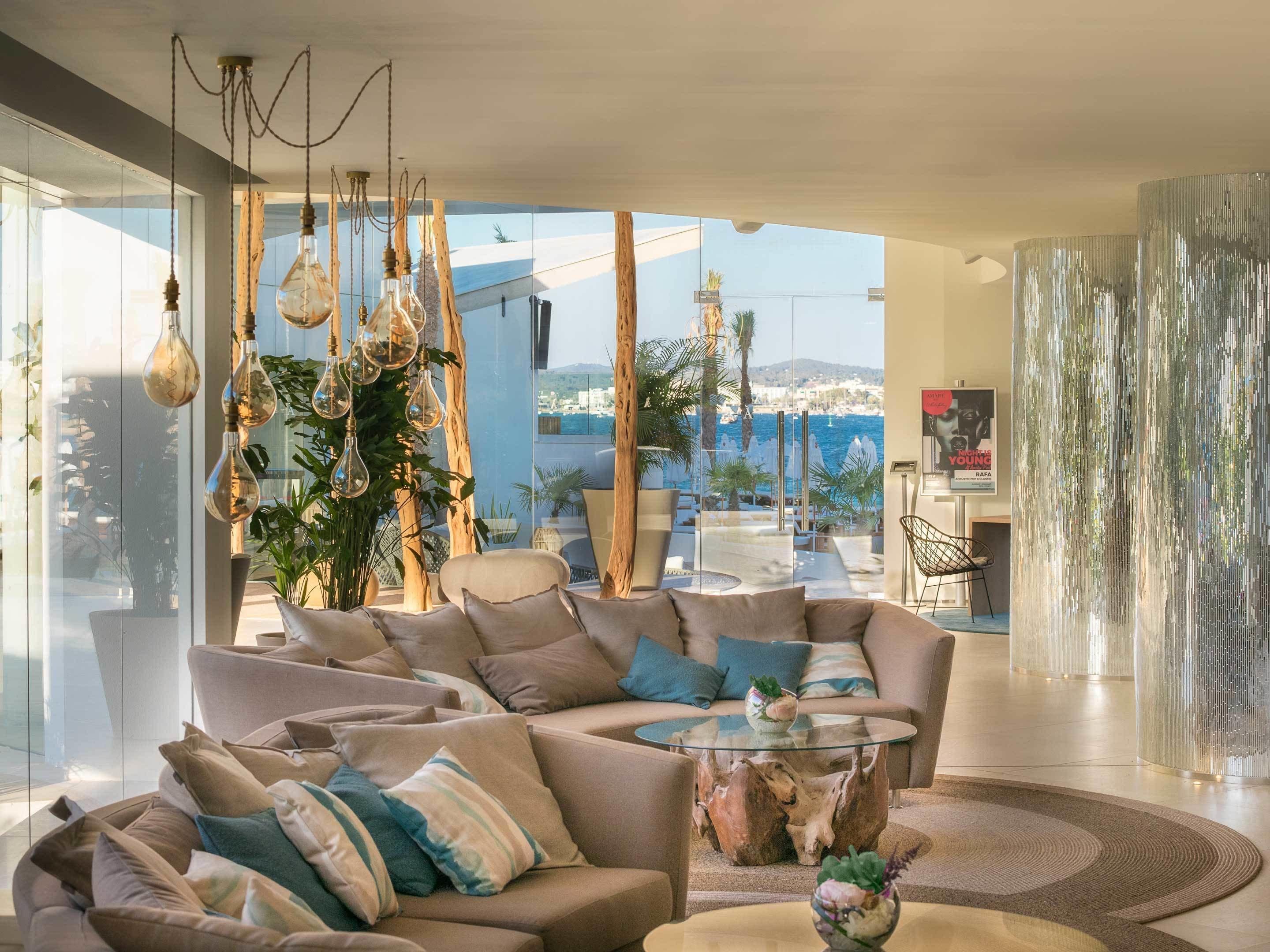 A modern living room with a large sofa, a glass coffee table, and hanging light fixtures.