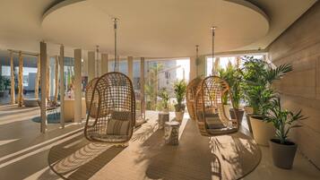 Een moderne lobby met hangende rieten stoelen, potplanten en een rond vloerkleed.